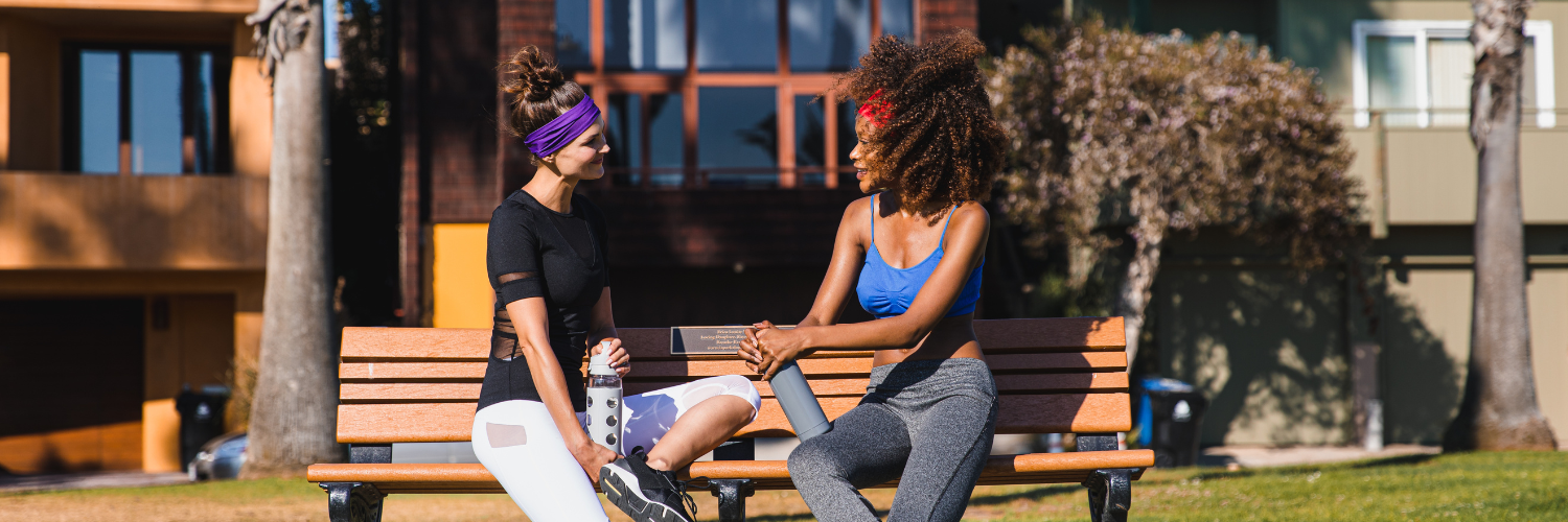Two women wearing Suddora headbands talking on a bench